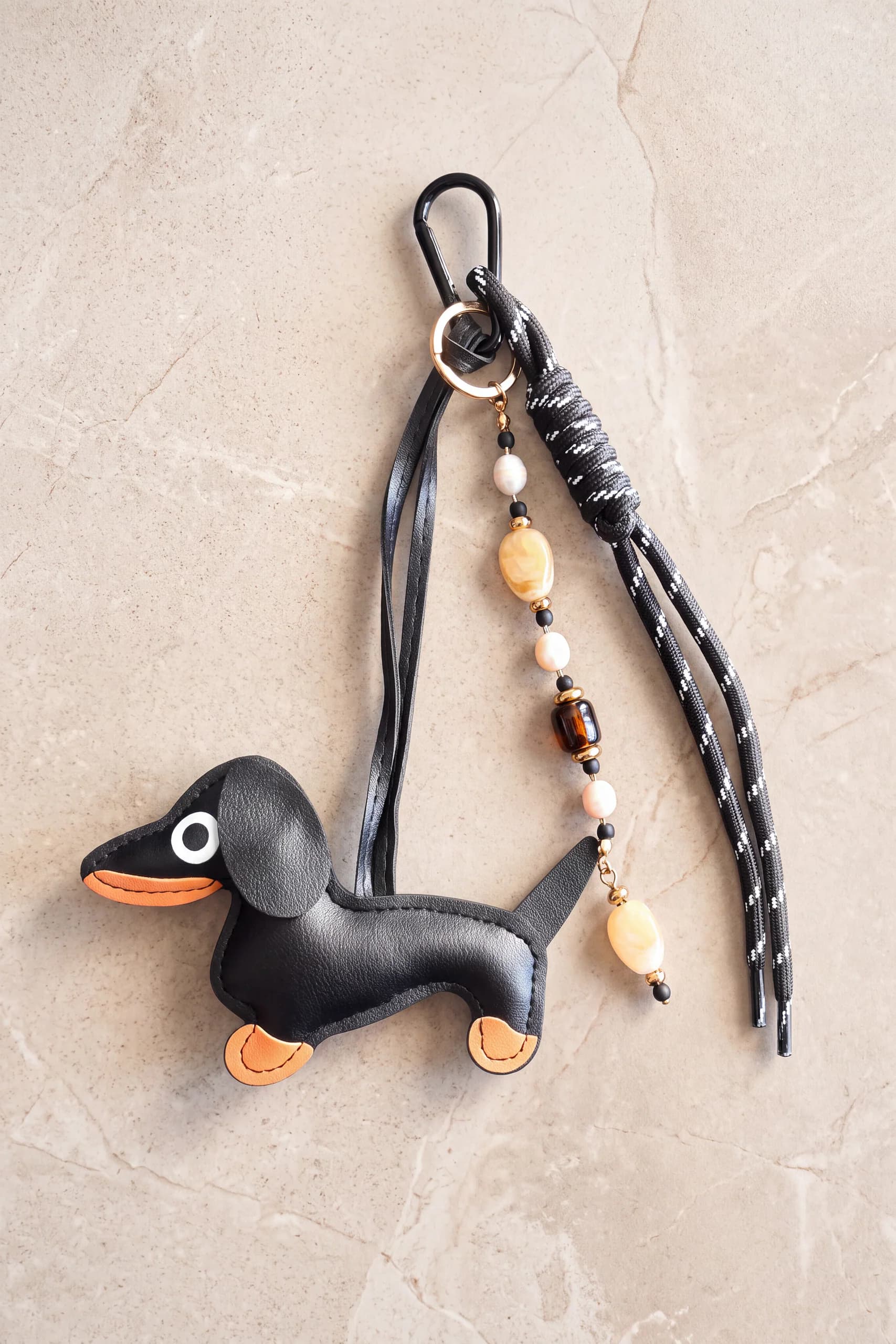 Charm de mala em forma de salsicha preto em pele sintética PU, com mosquetão, cordão preto de paracord e pendente de pérolas, contas cor de âmbar e contas pretas sobre pedra clara